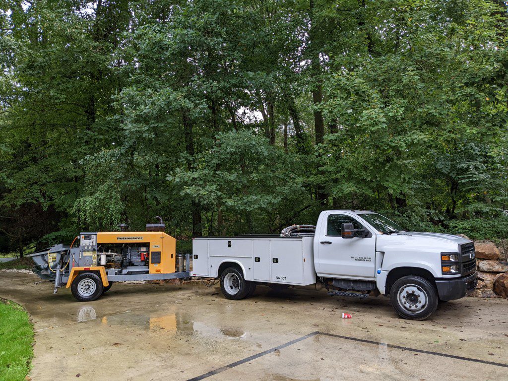 White truck with yellow tow-behind concrete pump
