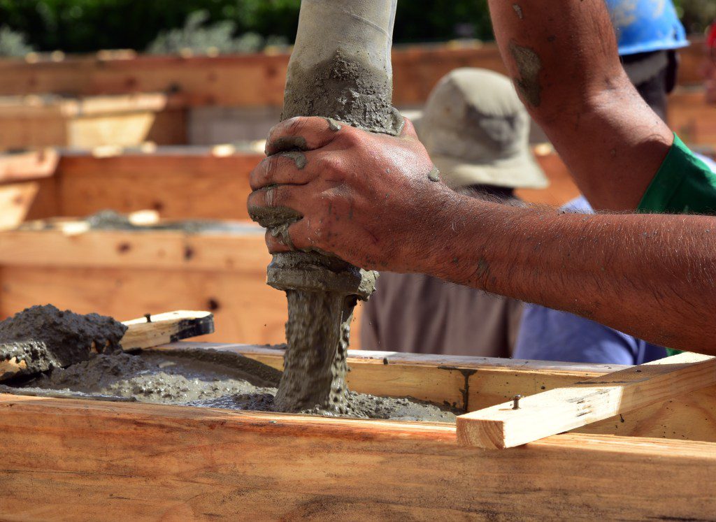 A man uses a hose to pour concrete into a block fill.